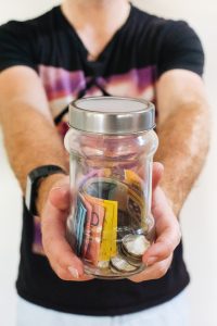 person holding out glass jar with money